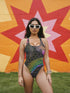 Holographic snake scale one-piece swimsuit featuring hexagon pattern with electric green, purple and blue scales on black background. Cheeky cut with scoop neck and low back design. Alternative gothic swimwear perfect for festivals, raves, beach parties. Available XS-3X, UPF 50+ protection with moisture-wicking fabric.